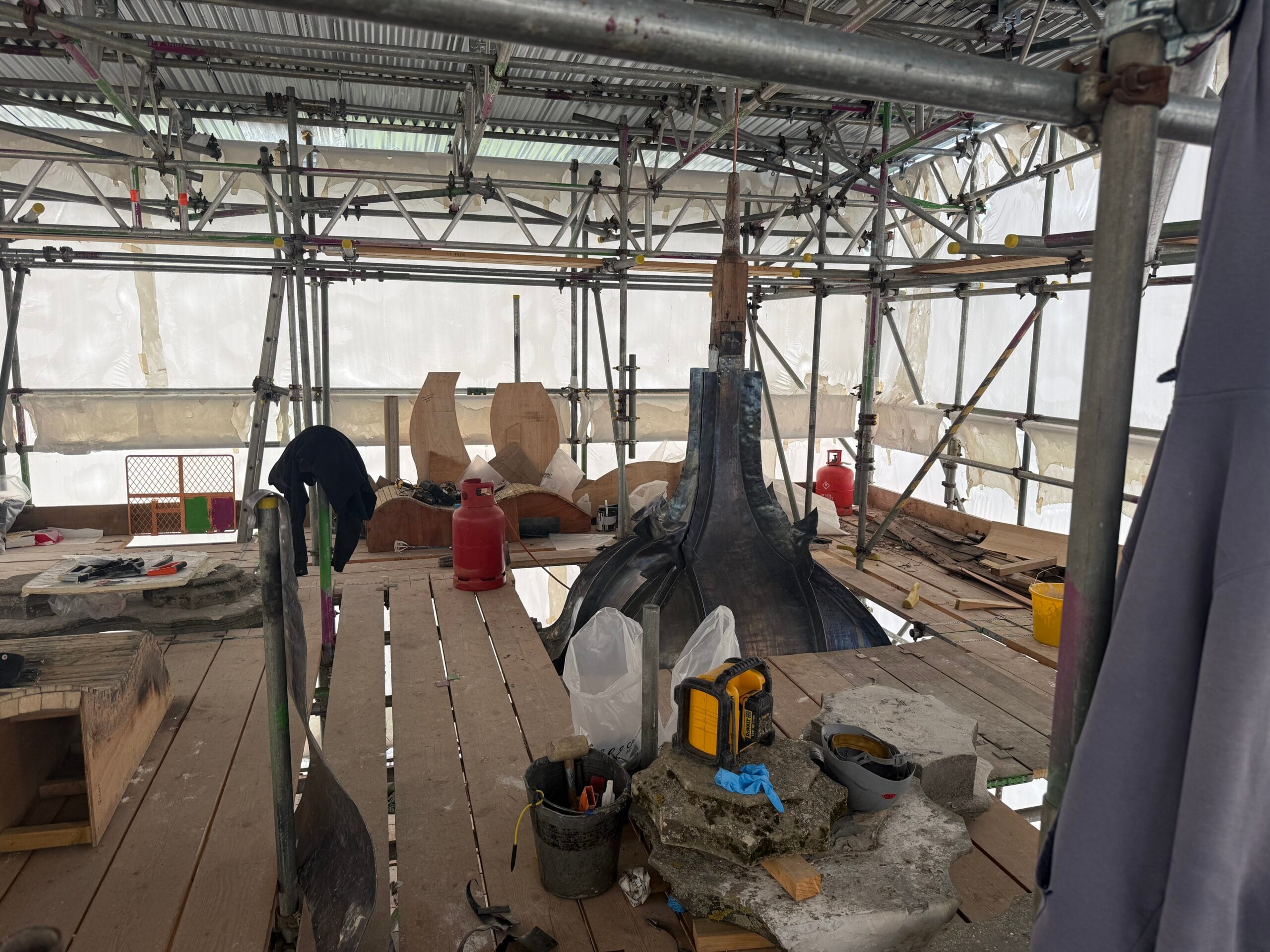 Work underway beneath the temporary roof, with stone, timber and lead work taking place across the scaffold.